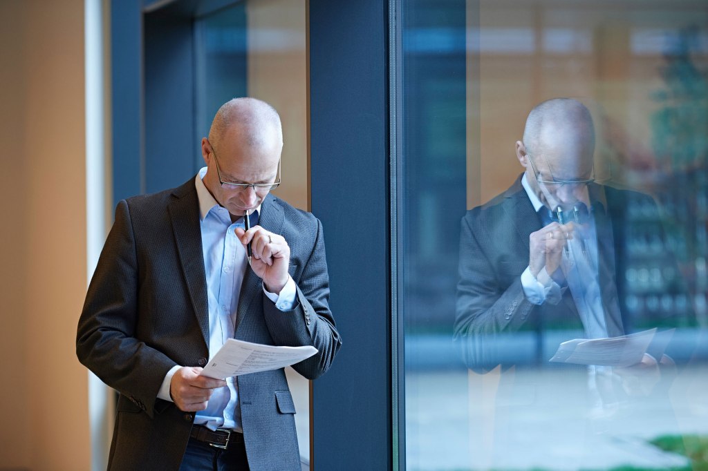 Mature businessman by office window reading paperwork
