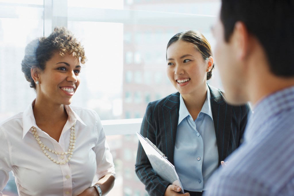 Three co-workers smiling, standing and connecting in and office